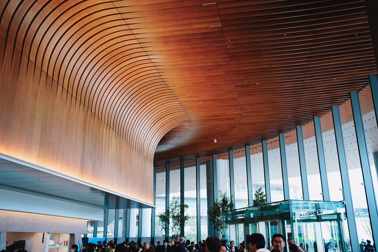 People gather in a modern hall with a curved wooden ceiling.