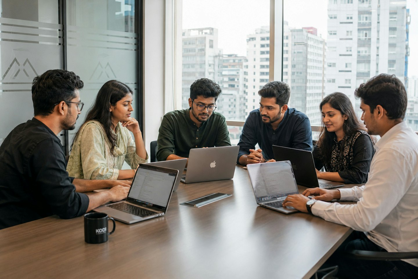 Young professionals collaborating around a table with laptops and city view.